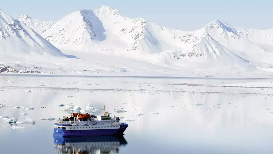 Small cruise ship cruising through the icy waters in front of breathtaking white mountains. 