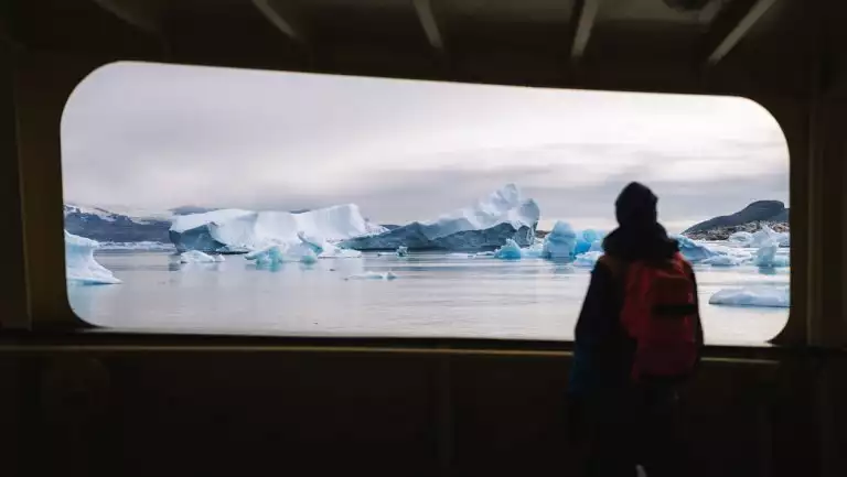 West Greenland traveler on the Disko Bay to Uummannaq cruise stands on deck of ship & views blue icebergs.