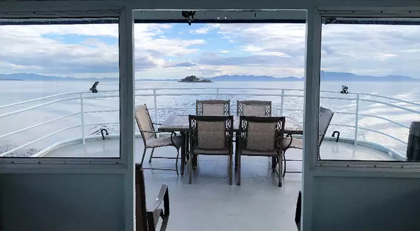 View of the stern of an Alaska yacht charter ship through a covered doorway showing back deck seating while the ship is at sail