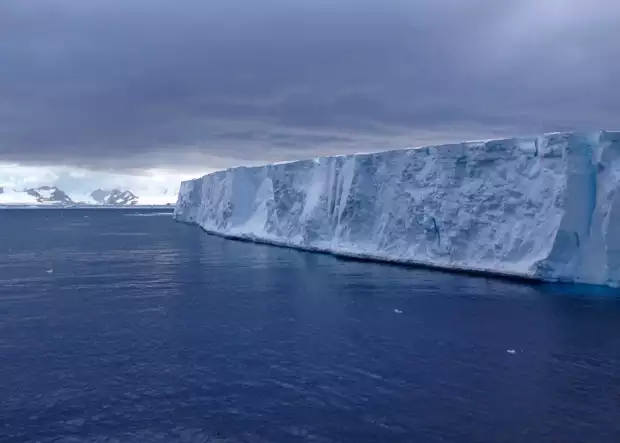 A tabular iceberg seen from its profile amid a dark stormy sky