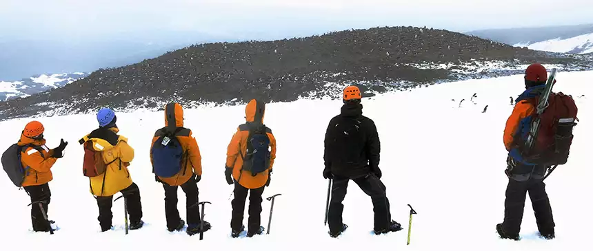 Group taking a break from their mountaineering excursion and looking at the view of hundreds of penguins from where they climbed in Antarctica.