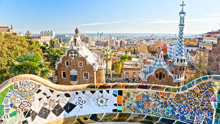 View from colorful tiled Park Guell overlook in Barcelona, Spain with brick & blue & white buildings below.