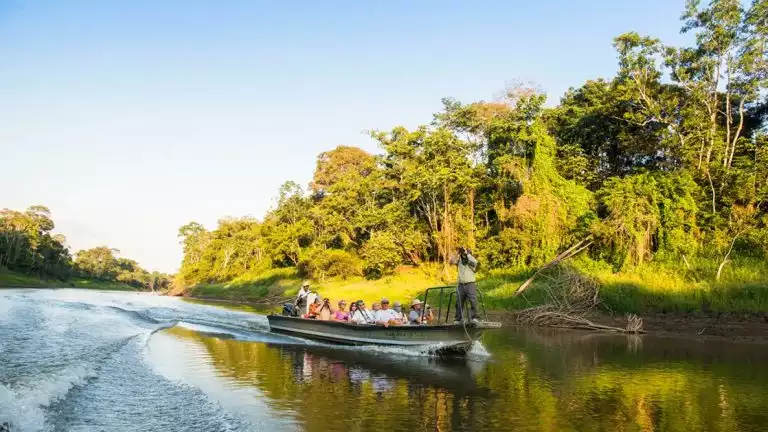 Small river boat filled with travelers and a guide exploring the upper amazon on a bright sunny day