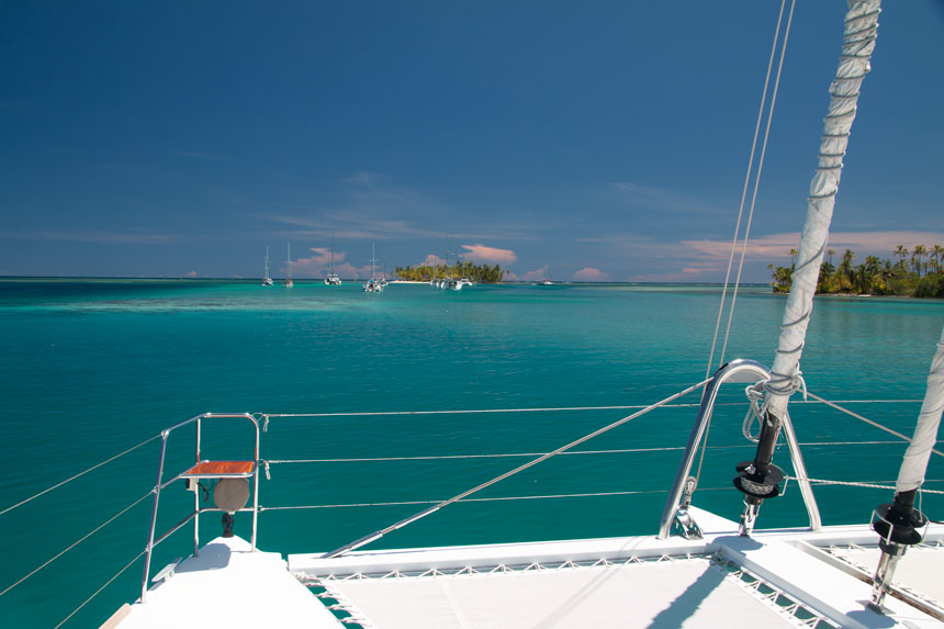 View from trampoline net bow of a white catamaran cruising turquoise waters among tropical islands on a Panama cruise.