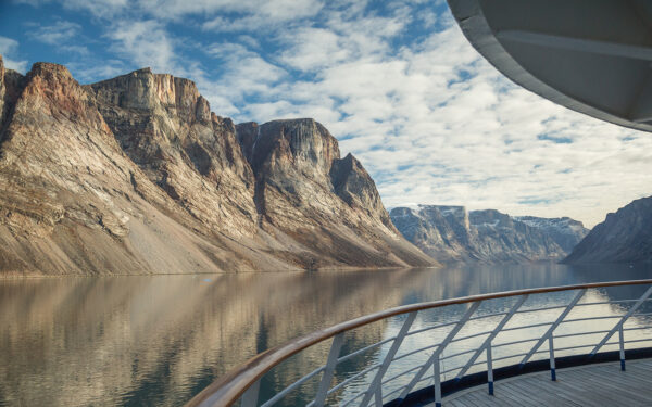 View from a Northwest Passage cruise ship showing the ship railing and the still water and steep mountainsides