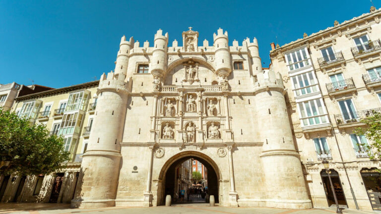 Santa maria arch in burgos that looks like a historic castle with small green trees on the ground on a sunny day