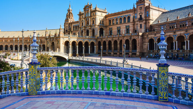Blue-tile bridge over a turquoise moat surrounded by a circular beige brick building in Seville, Spain, seen on the Med Feast cruise.