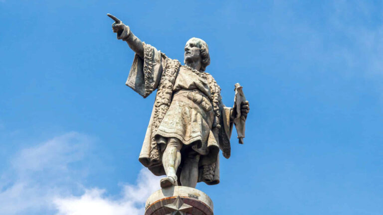 Statue of christopher columbus pointing as a monument to him, infront of a blue sky and light clouds