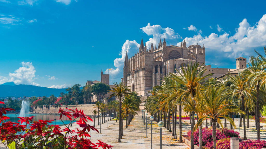 Beautiful walkway leading you to a cathedral with pink and red flowers and palm trees overlooking a large fountain