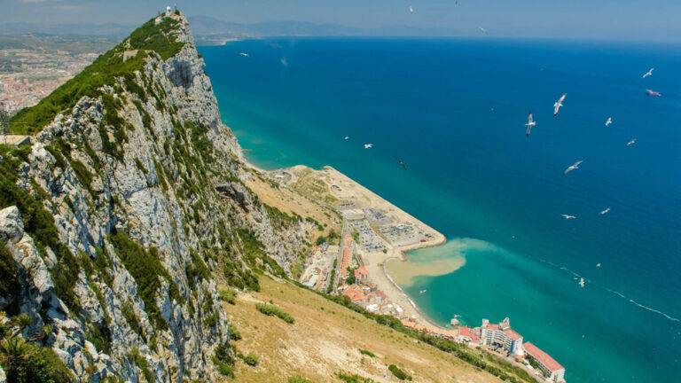 Overlook of Gibraltar rock looking down at the bright blue waters below with boats cruising around