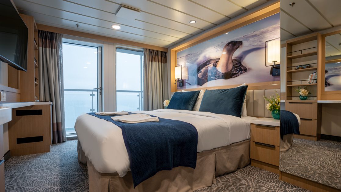 double bed aboard small ship cruise in antarctica with blue and white tones and floor to celling windows and balcony