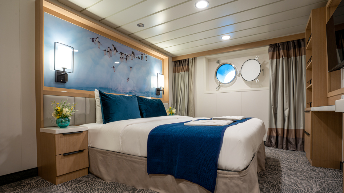 double bed aboard small ship cruise in antarctica with blue and white tones and porthole window