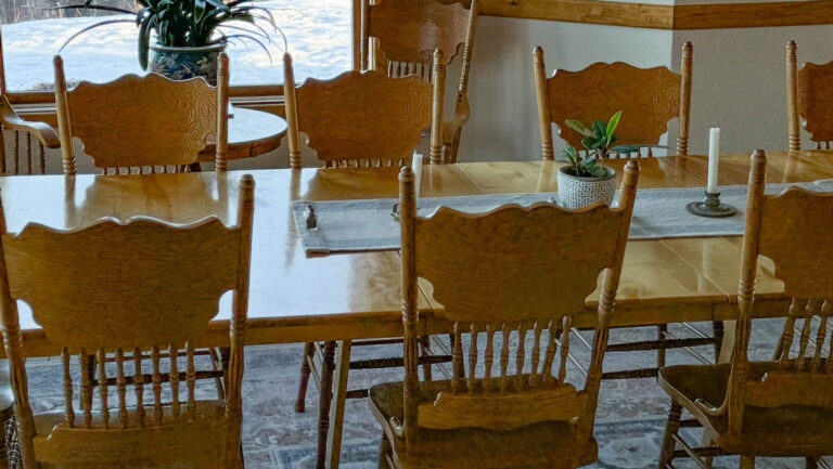 Long wooden dining room table & chairs beside view window of snowy Alaskan yard at the Denali Overlook Inn in Talkeetna.