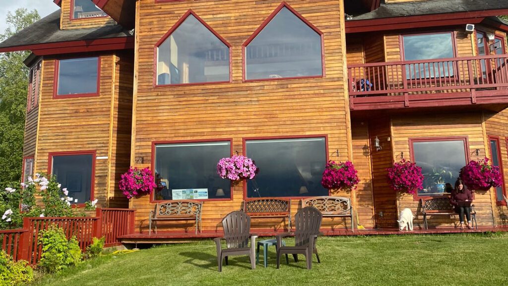 Exterior of Denali Overlook Inn with 3 floors, wood sideboards, multiple view windows, hanging flower baskets, deck & lawn.
