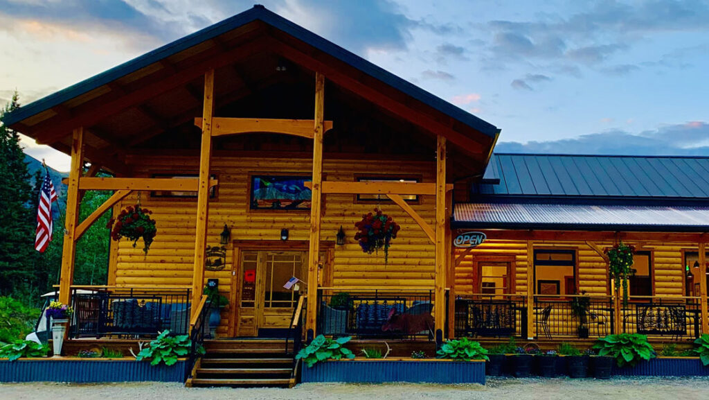 Exterior of large wooden cafe building with flowers & planter boxes beside wraparound deck, at McKinley Creekside Cabins.