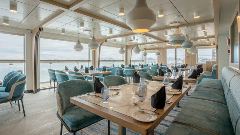 Dining area aboard small ship cruise with floor to ceilings windows and views of antarctica