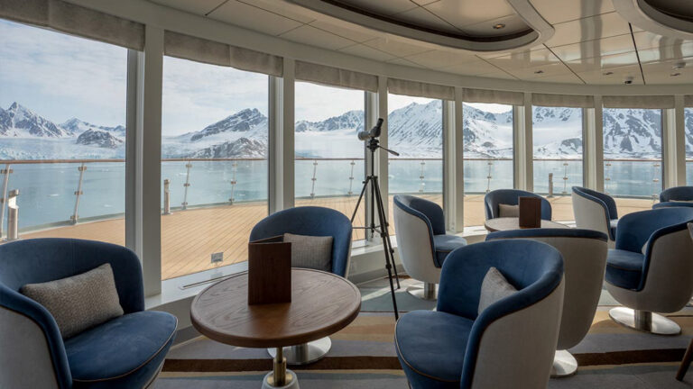 Seating area with blue chairs and white pilllows aboard ocean albatros on a sunny day looking out into antarctica