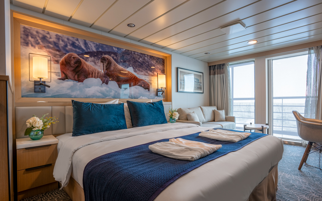 double bed aboard small ship cruise in antarctica with blue and white tones, floor to celling windows with a balcony off the room