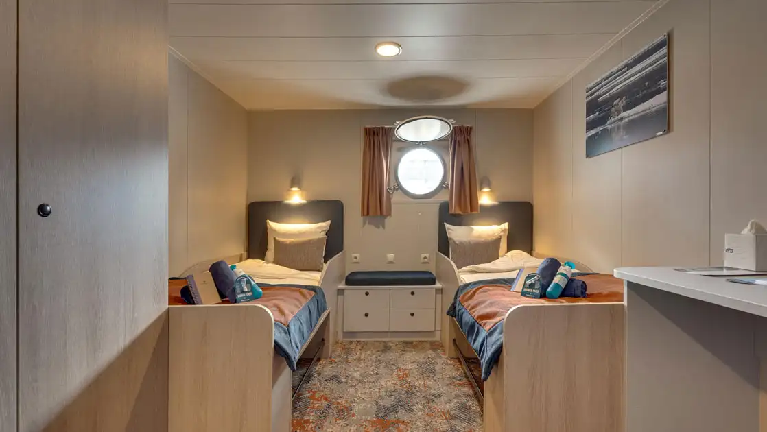 cabin with 2 beds and a porthole aboard Plancius polar ship
