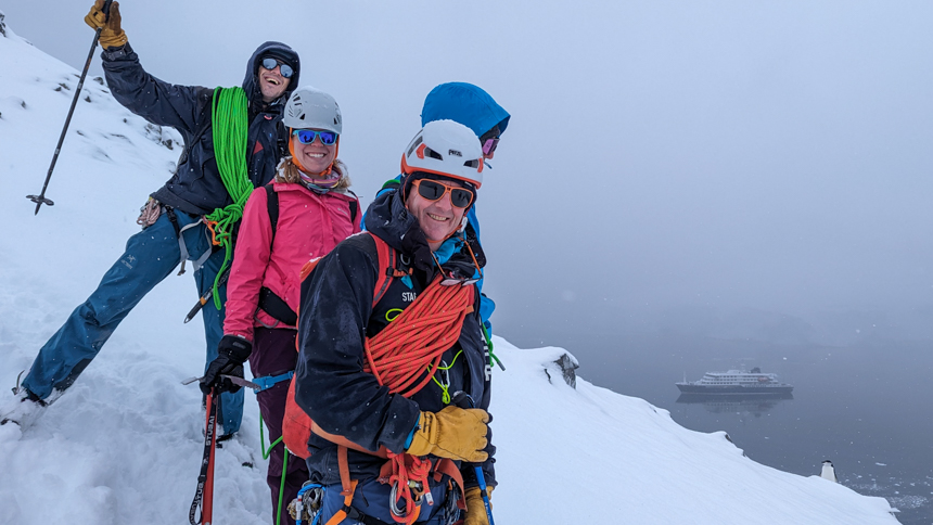 Mountaineers pictured on the top of the mountain exploring off the small expedition ship next to a penguins