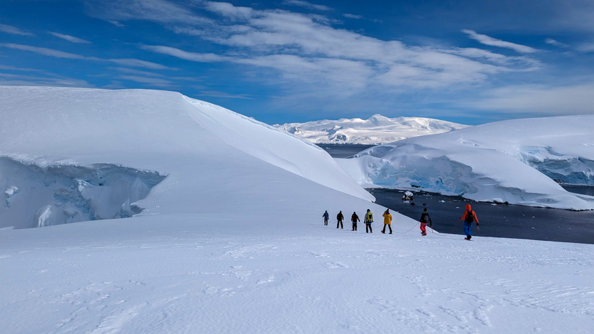 Mountaineers walk in a line on top of the icy snowy landscapes of Antarctica