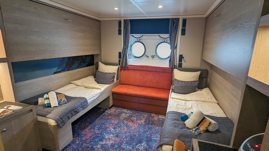 Quad porthole cabin aboard small expedition ship with two twin beds and porthole windows