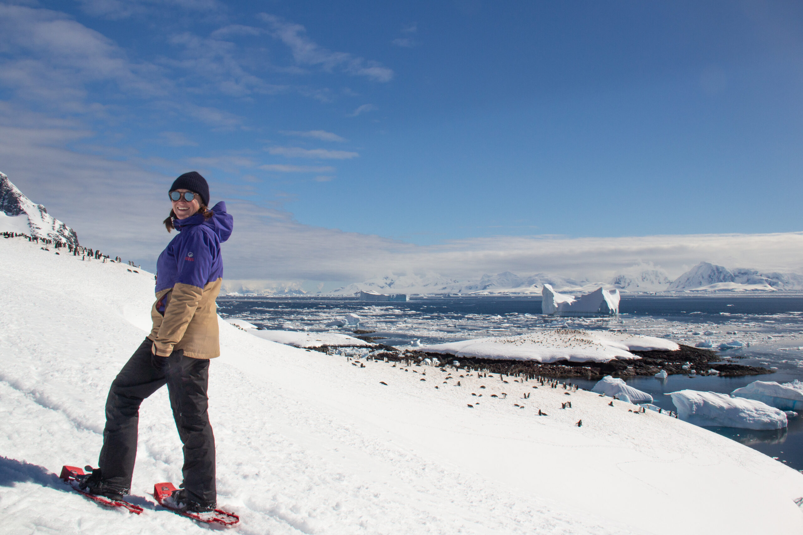 Women snowshoing though the Antarctica hills looking down on a colony of penguins
