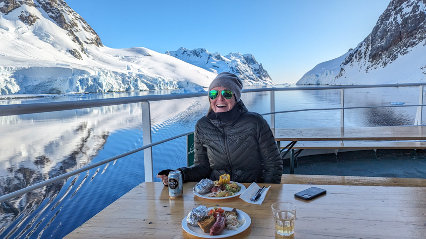 Women sitting on the outdoor deck enjoying a nice outdoor BBQ meal with winter clothes on cruising next to beautiful snowy mountains