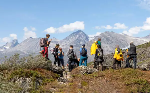 A group of adventure travelers stand high atop mountain range in Greenland looking at landscape that surrounds them.