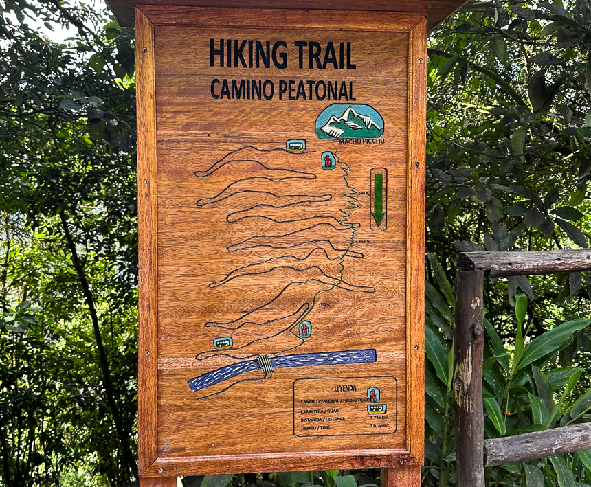 Large wooden sign with carved map of colored hiking route and bus route from Aguas Calientes to Machu Picchu citadel.