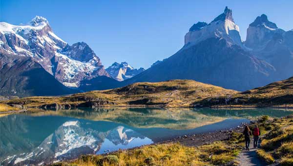 Two travelers seen on a lakeside trail on guided trip to Patagonia with the iconic sharp peak mountains behind them