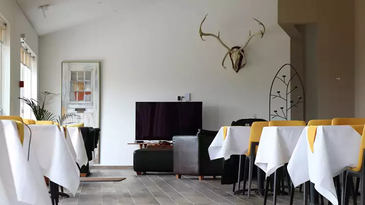 Restaurant at Hotel 1001 Nott in Iceland with 2-top tables in white & yellow cloth, reindeer head & antlers, & wall of windows.