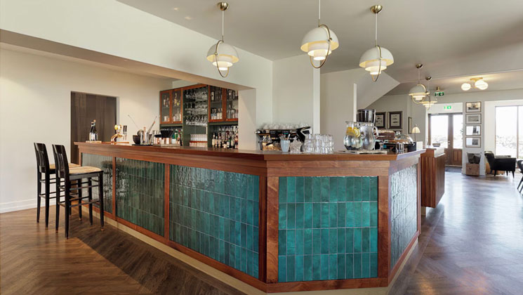 Bar of Hotel Budir in Iceland with teal tiles & wood edges, modern stools, pendant lighting, wood floors & open space.