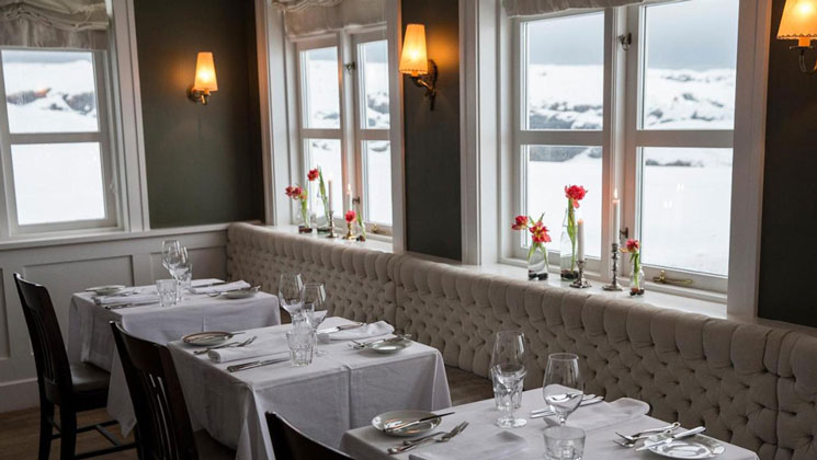 Dining room at Hotel Budir in Snaefellsnes Peninsula, Iceland, with gray bench & chair seating for 2-top tables in white cloth.