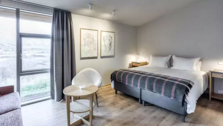 Guest room at Iceland's Hotel Husafell with double bed in white linens, framed art, modern white table & chair & view window.
