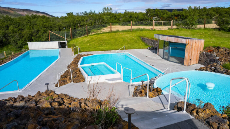 Manmade pools show teal among bright green grass on a sunny day at Iceland's Hotel Husafell.