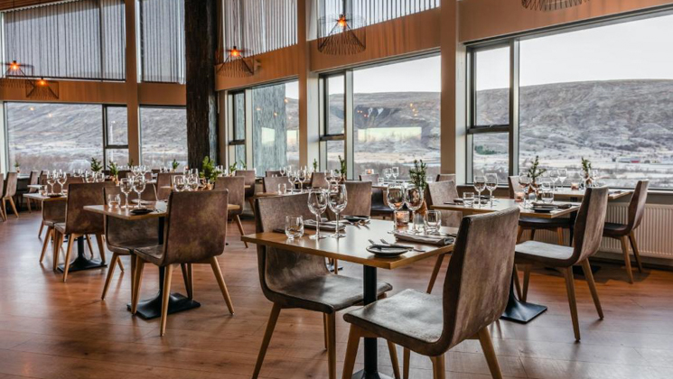 Restaurant at Hotel Husafell in Iceland with 2 stories of large windows, modern leather chairs, wood floors & 2- & 4-top tables.