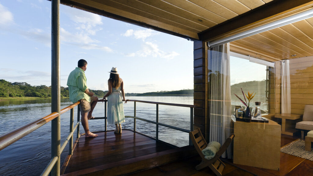 A traveling couple leans on the rail of their private balcony aboard a trip to Peru on the Amazon River