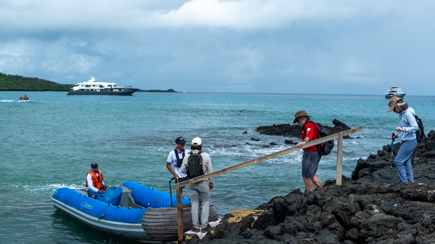 Guests walking on lava rock to board zodiac to be transferred back to small ship on a cloudy day