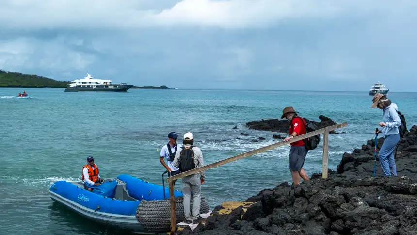 Guests walking on lava rock to  board zodiac to be transferred back to small ship on a cloudy day 