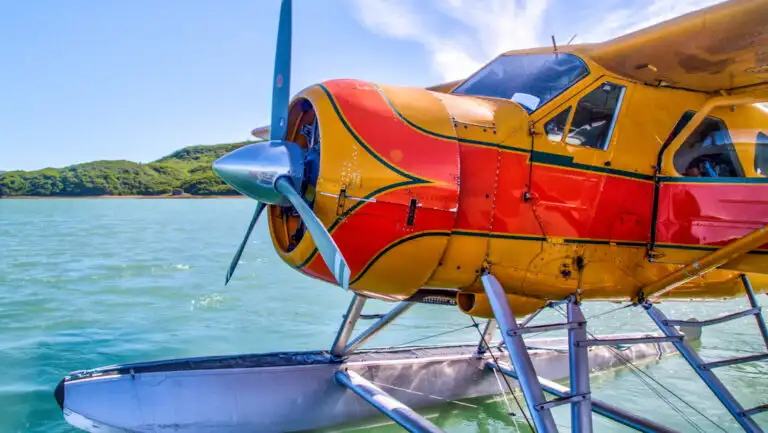 Floatplane in bright yellow & orange sits in calm teal water on a sunny day in Alaska during a grizzly bear photography tour.
