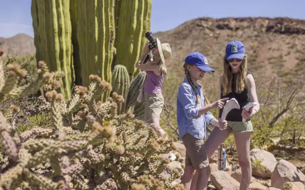 Two young girls point at an animal bone while their mother takes a picture of a cactus behind them