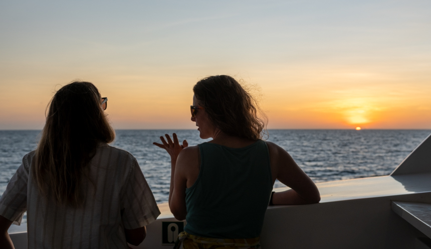 Two women chatting looking at the sun setting off small ship infinity in Galapagos