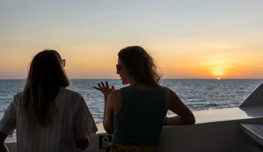 Two women chatting looking at the sun setting off small ship infinity in Galapagos 