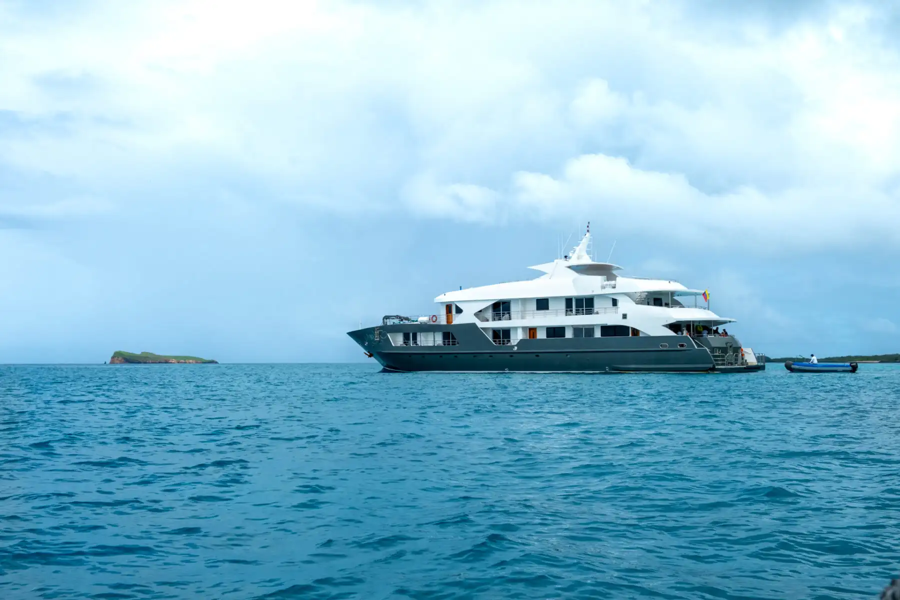White and grey Small ship infinity anchored in the Galapagos on a cloudy day next to a small island