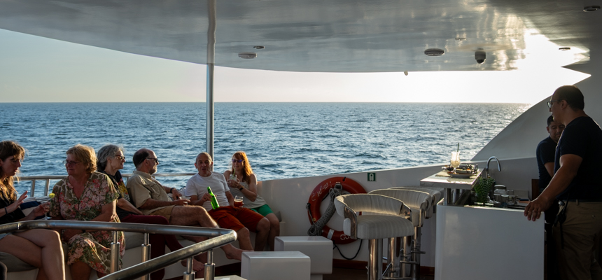 Bar on small ship infinity with guest enjoying a cocktail as they share stories with water surrounding the ship