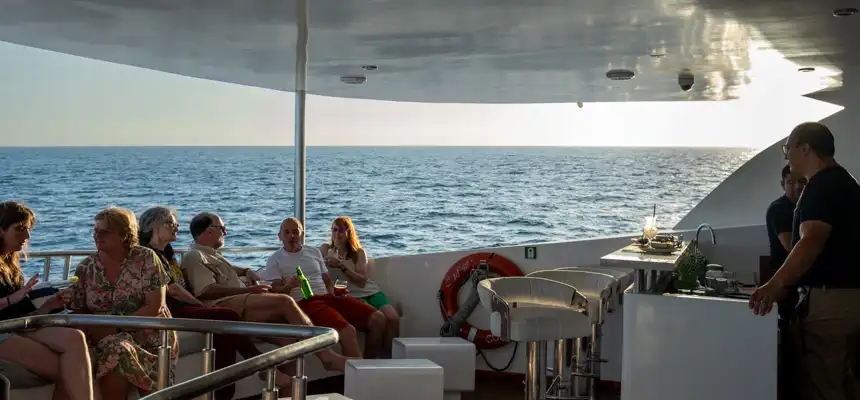 Bar on small ship infinity with guest enjoying a cocktail as they share stories with water surrounding the ship 