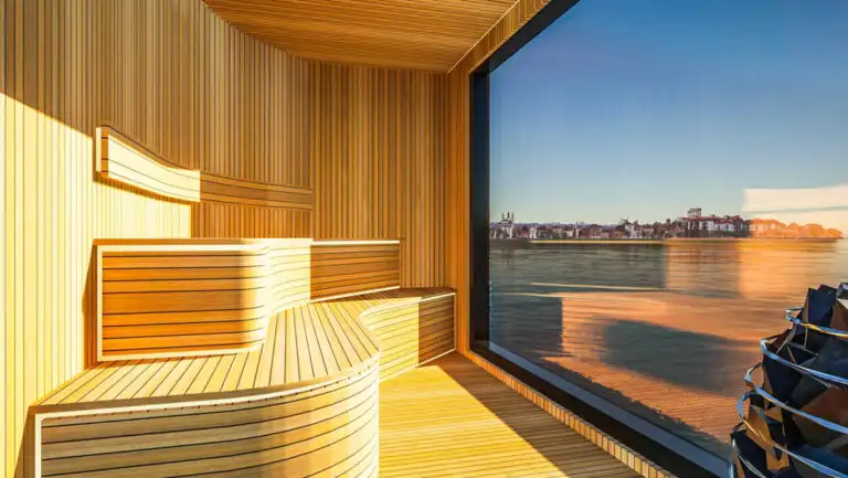 Wood sauna with 2 curved benches & hot rocks beside wall of glass aboard National Geographic Connect riverboat in Europe.