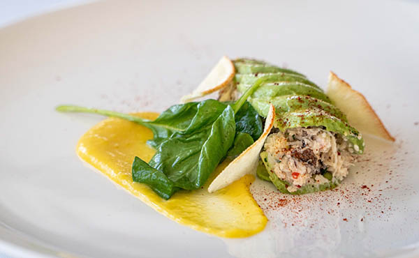 A detail view of crab timbale appetizer showing wilted spinach, yellow mango reduction and avocado wrapped crab