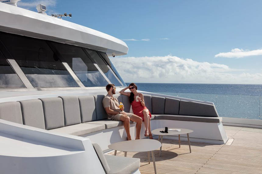 The curved bow bench seating with tables aboard Hermes and a couple sitting with drinks on it